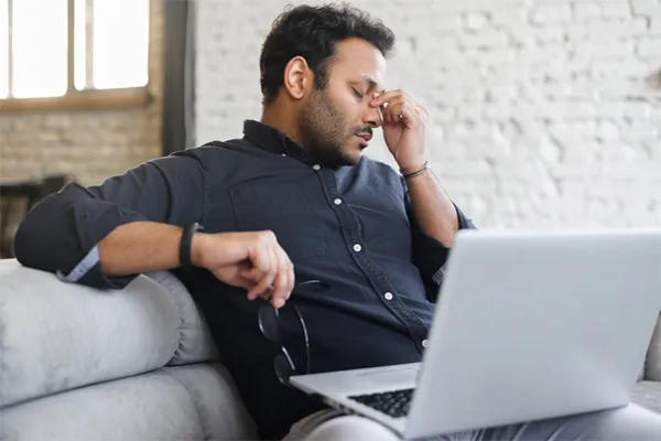 Anxiety-Clinic A man using a laptop pinches his forehead with tension. Get anxiety treatment from Jennifer Jose-Cappola, MD in Stamford.
