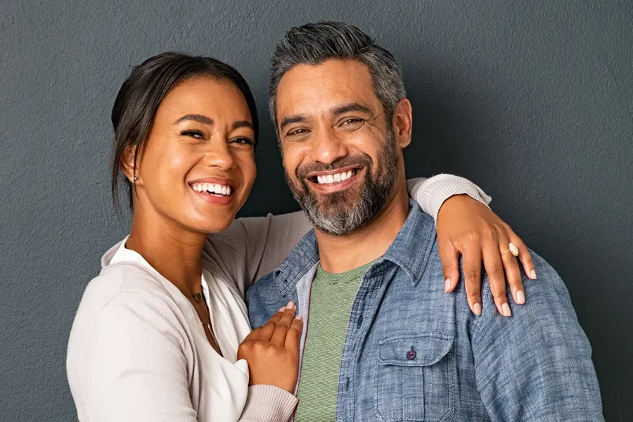 Bioidentical-Hormone-Therapy-Doctor A middle-aged couple with their arms around each other standing against a gray background and smiling, happy with the bioidentical hormone therapy they received from Jennifer Jose-Cappola, MD in Stamford.