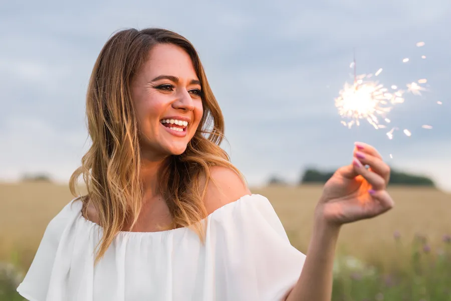EMsella-for-Women-Clinic A cheerful young woman holding a lit sparkler in an open field at dusk satisfied with successful EMsella Pelvic Floor Strengthening treatment by Jennifer Jose-Cappola, MD in Stamford.