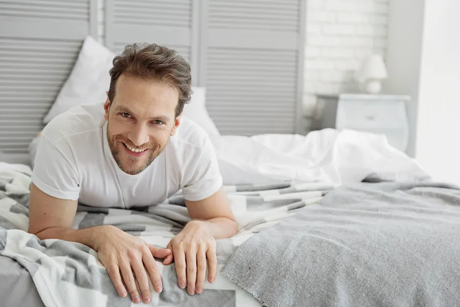 Low-Libido-in-Men-Doctor A dirty-blonde haired man lays on his stomach in bed smiling. Schedule treatment for low libido in men from Jennifer Jose-Cappola, MD in Stamford.
