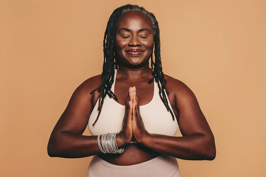 Obesity-Clinic An older African American woman confidently posing against a warm background smiling with hands in a prayer pose. Jennifer Jose-Cappola, MD treats obesity using functional medicine in Stamford.