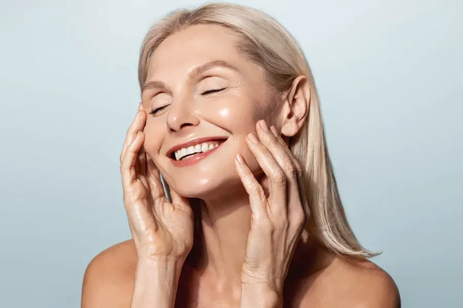PRP-Facelift-Facial-Doctor A beautiful mature blonde woman touches her face, happy with her PRP facelift and facial injections from Jennifer Jose-Cappola, MD in Stamford.