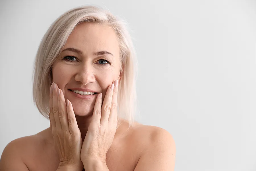 PRP-Microneedling-Clinic A mature woman touches her faces to feel the successful results of PRP microneedling and skin rejuvenation treatments from Jennifer Jose-Cappola, MD in Stamford.