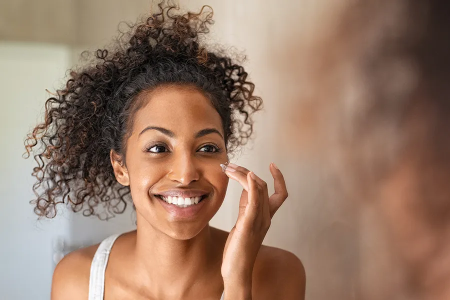Revision-Skincare-Clinic A beautiful mixed-race woman applies skin cream. Get Revision Skincare products from Jennifer Jose-Cappola, MD in Stamford.