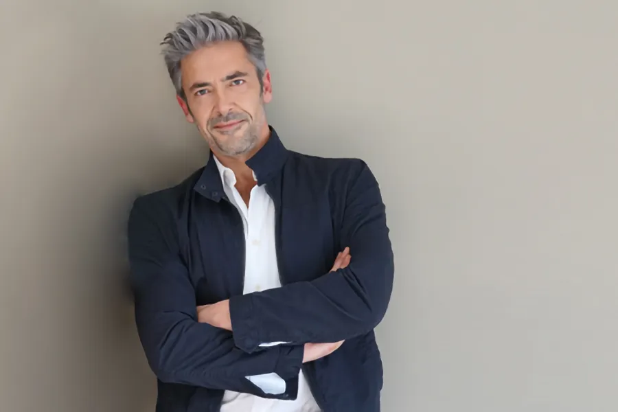 Testosterone-Low-T-Solutionsn-Clinic A middle-aged man in a white shirt and dark blue jacket leans against a gray wall smiling. Get testosterone for Low T from Jennifer Jose-Cappola, MD in Stamford.